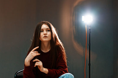 Portrait of beautiful young woman sitting in illuminated room