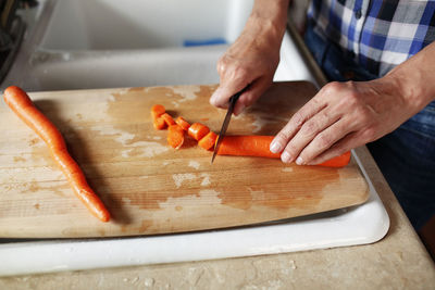 Close up of woman's hands cutting a carrot on a chopping block