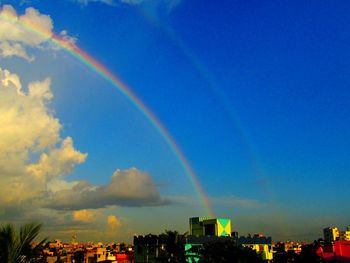 Rainbow over buildings in city against blue sky