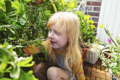 Happy girl sitting by plant in balcony