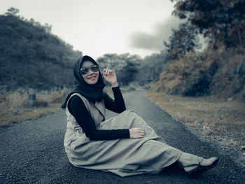 Portrait of woman wearing headscarf and sunglasses sitting on road