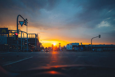 Silhouette city street against sky during sunset