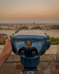 Close-up of coin-operated binoculars against cityscape during sunset