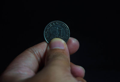 Close-up of hand holding coin against black background