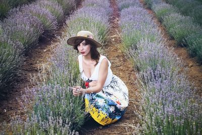 High angle portrait of young woman sitting by lavender plants on field