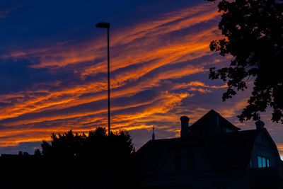 Low angle view of silhouette trees and buildings against sky during sunset