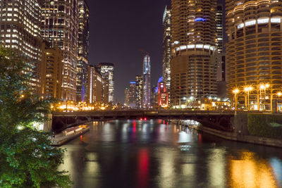 Illuminated bridge over river by buildings against sky at night