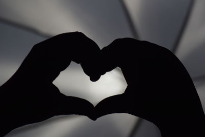 Close-up of silhouette hand holding heart shape against black background
