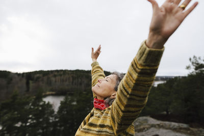 Carefree female hiker with arms raised on mountain against sky