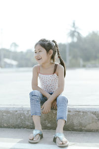 Full length of cheerful girl sitting on retaining wall
