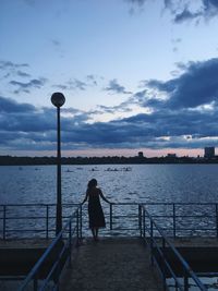 Woman standing on railing by sea against sky