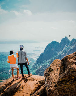 Rear view of men standing on rock by mountain against sky