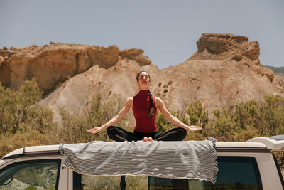 Low angle view of woman meditating while sitting on car roof