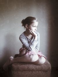 Thoughtful girl with hand on chin sitting on footstool