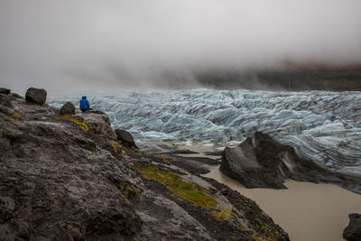 Man sitting on rock formation by icebergs