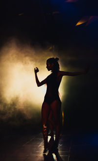 Silhouette of a woman dancing between lights and smoke unrecognozible person