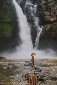 Young woman standing against waterfall