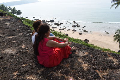 Side view of woman sitting on rock at beach