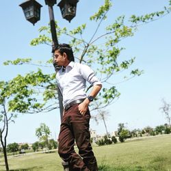 Low angle view of young man standing by street lamp on field against sky