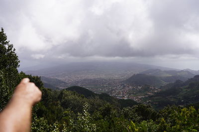 Cropped image of hand against plants and mountain against sky