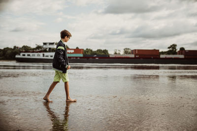 Side view of boy standing in boat against sky