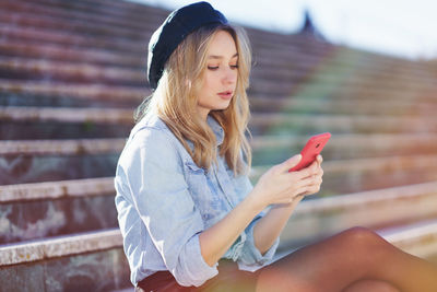 Beautiful young woman using mobile phone while siting outdoors