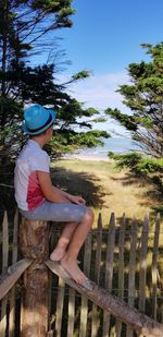 Midsection of woman sitting by fence against sky