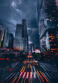 Illuminated city street by buildings against sky at night