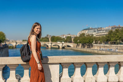 Portrait of smiling young woman standing by bridge against sky