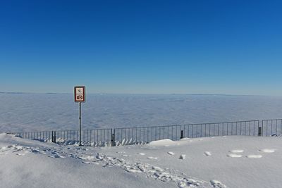 Road sign by sea against clear blue sky