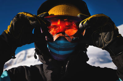 Portrait of a skier holding on to his mask on the ski slope. close-up against a clear blue sky and