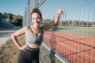 Portrait of young woman standing on chainlink fence