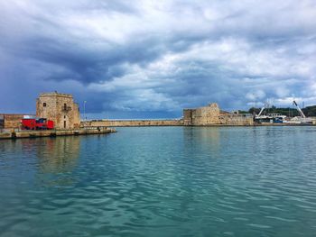 View of buildings by sea against cloudy sky