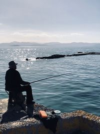 Silhouette man fishing in sea against sky