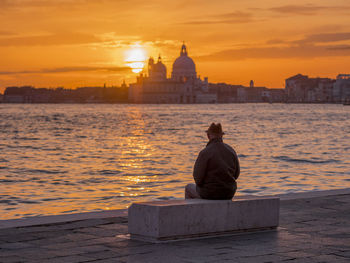 Rear view of man standing by sea against sky during sunset