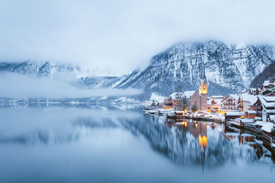 Scenic view of lake by buildings against sky during winter