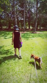 Rear view of woman walking with dog on grass