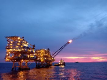 Illuminated ship in sea against sky at sunset