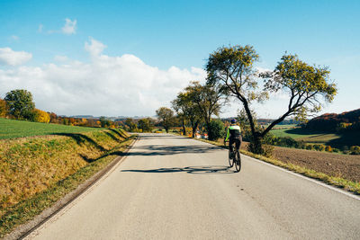 Rear view of woman riding bicycle on road against sky