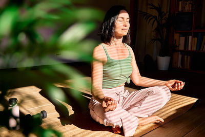 Woman practicing yoga and meditation at home sitting in lotus pose relaxed with closed eyes.