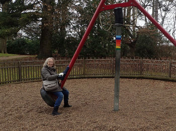 Happy mature woman playing on swing in playground during winter