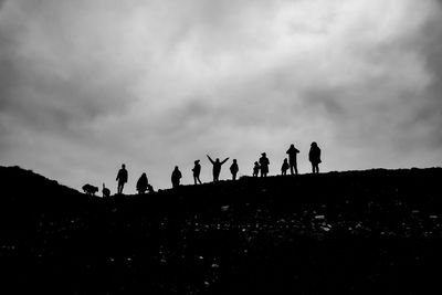 Silhouette people walking on field against cloudy sky