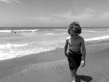 Full length of shirtless boy playing on beach against sky