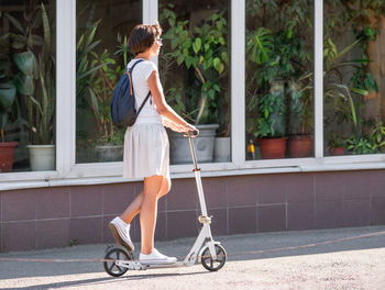 Woman rides kick scooter. tropical plants for landscaping in flower shop. eco-friendly transport. 