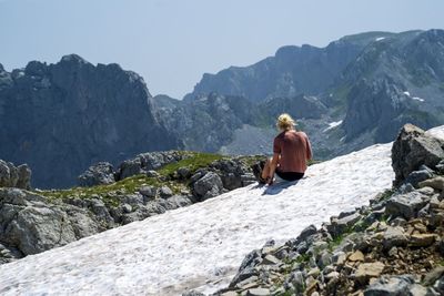 Rear view of man sitting on rocks against mountains