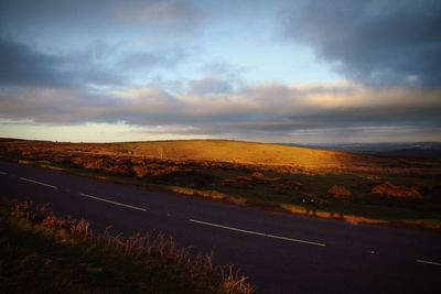 Road by landscape against sky during sunset