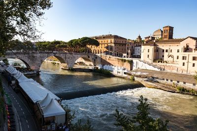 Arch bridge over river amidst buildings against sky