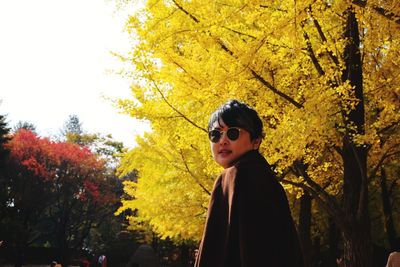 Young man wearing sunglasses standing by trees against sky