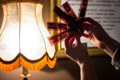 Cropped hands of woman holding film reel against illuminated lamp