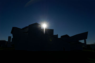 Low angle view of sunlight streaming through silhouette building against sky